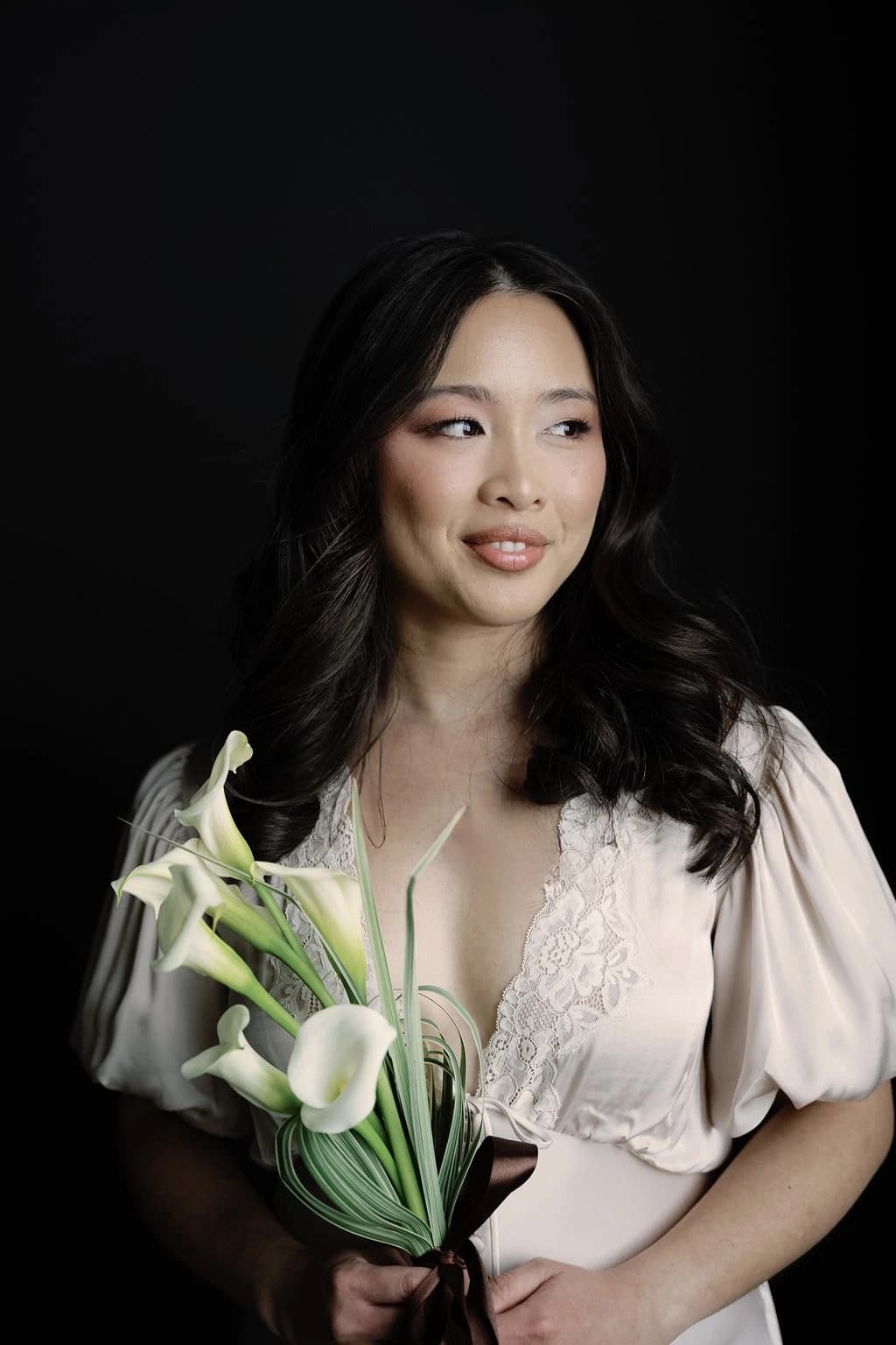 San Le, founder of Vivid Moments with San, in an ivory lace dress holding a bouquet of white calla lilies