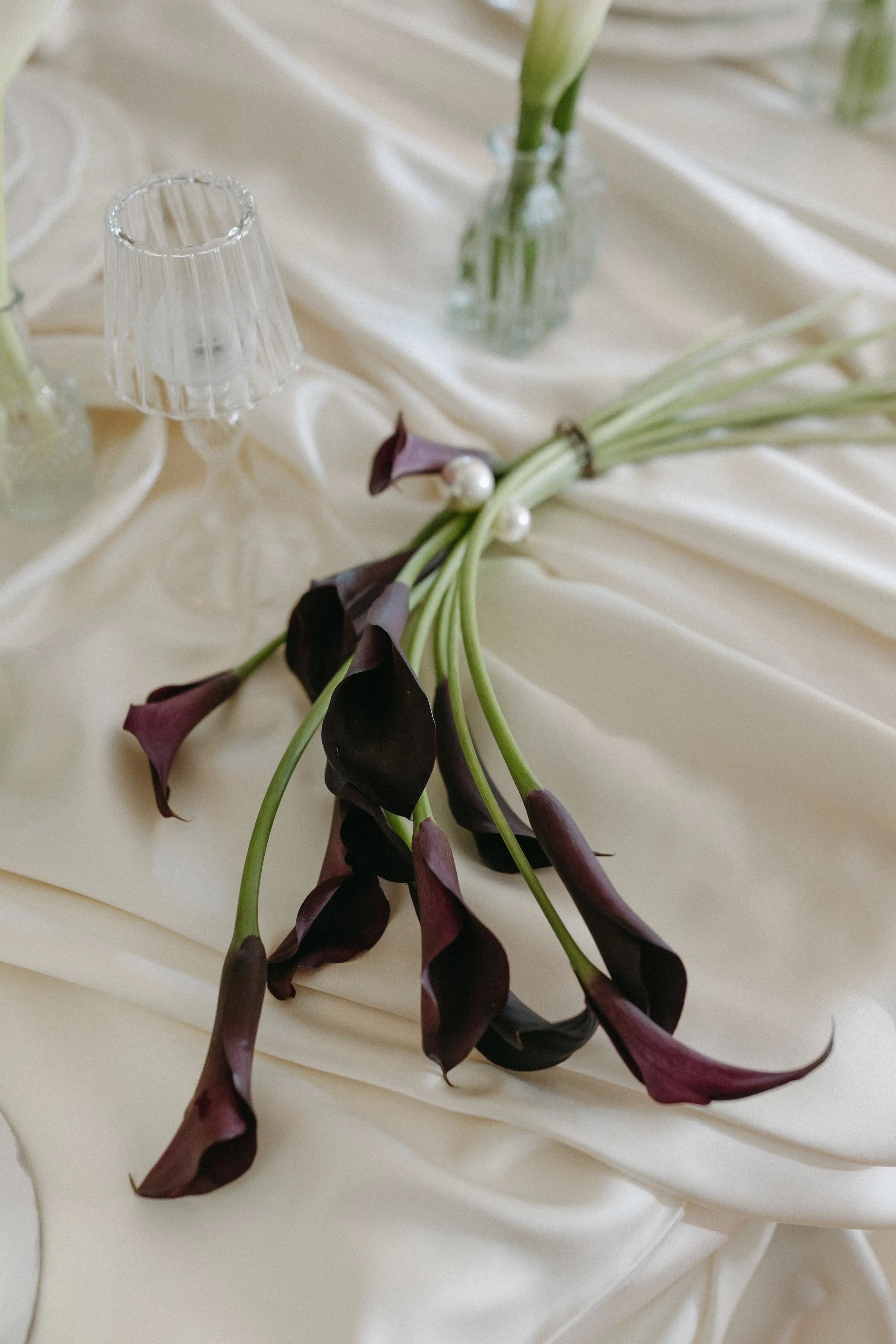 Deep burgundy calla lilies resting on ivory silk