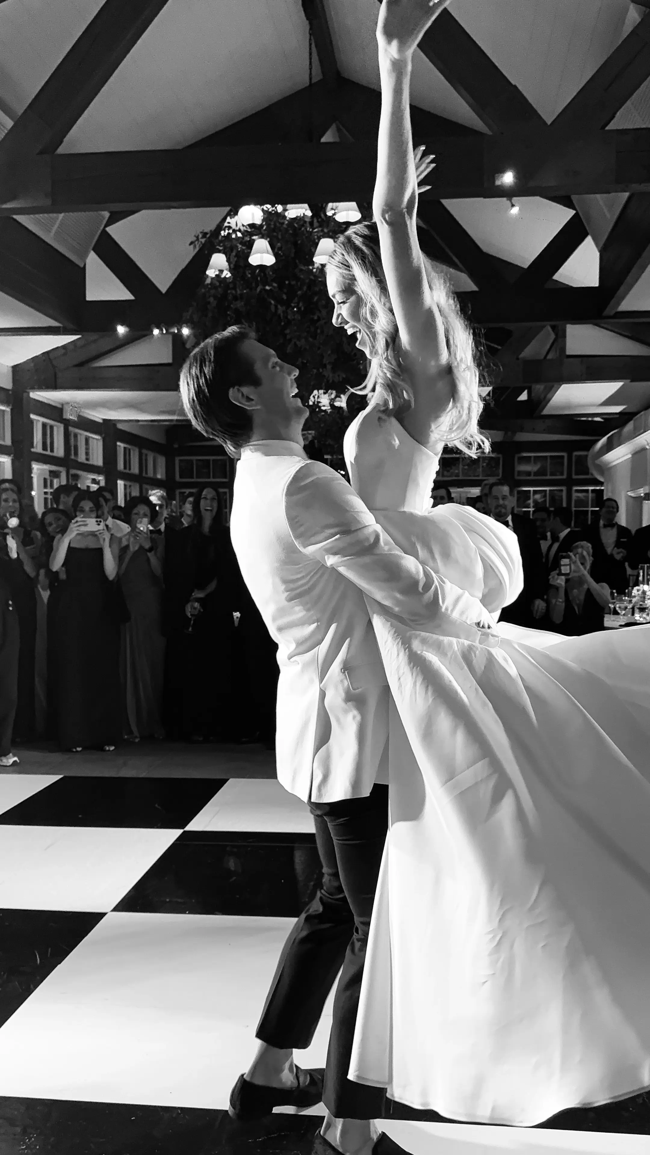 A couple dancing on a checkered floor, the bride's arm raised mid-spin