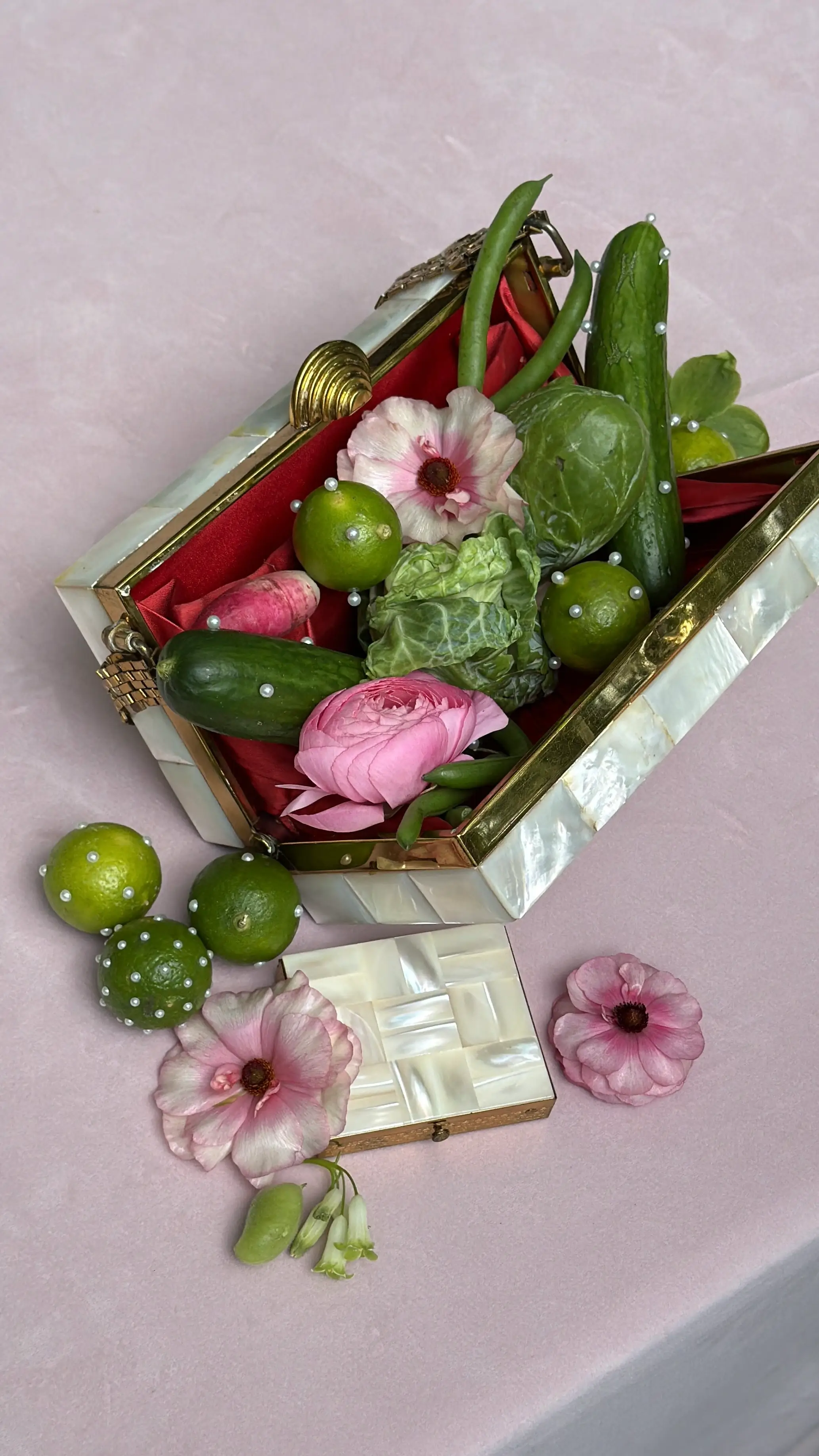 A vintage jewelry case holding rings and earrings, surrounded by pink and green blooms